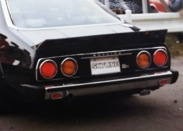 Rear view of a vintage black Nissan Skyline car with distinct round taillights and a visible Skyline license plate.