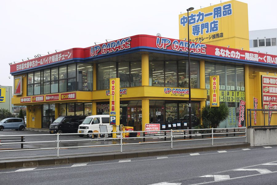 Exterior of UP GARAGE store specializing in used car parts and accessories in Japan, with signs in Japanese.