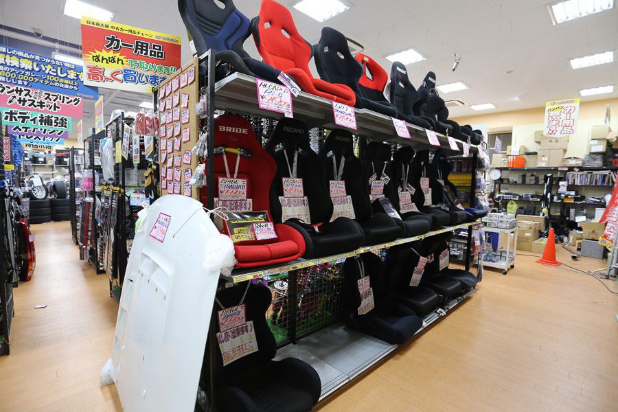 Rows of car racing seats on display in an auto parts store. Signage in Japanese with 高く買います meaning high purchase price.