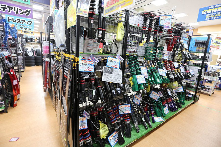 A well-organized display of automobile suspension and parts in a Japanese auto shop. Signs are written in Japanese.
