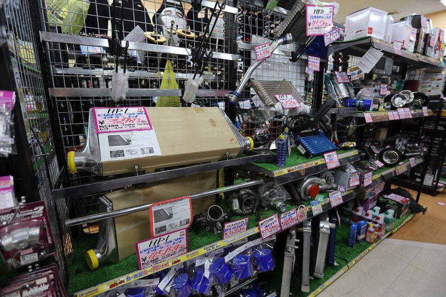 Auto parts store showcasing various car accessories and performance parts with Japanese retail signs displayed on shelves.