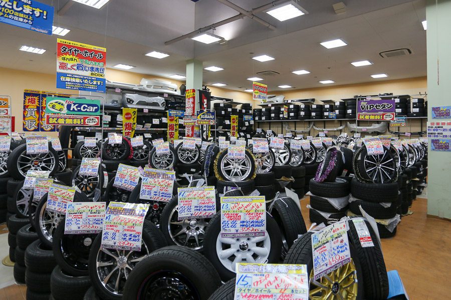 A tire and wheel shop in Japan featuring various alloy wheels neatly stacked with handwritten signs in Japanese.