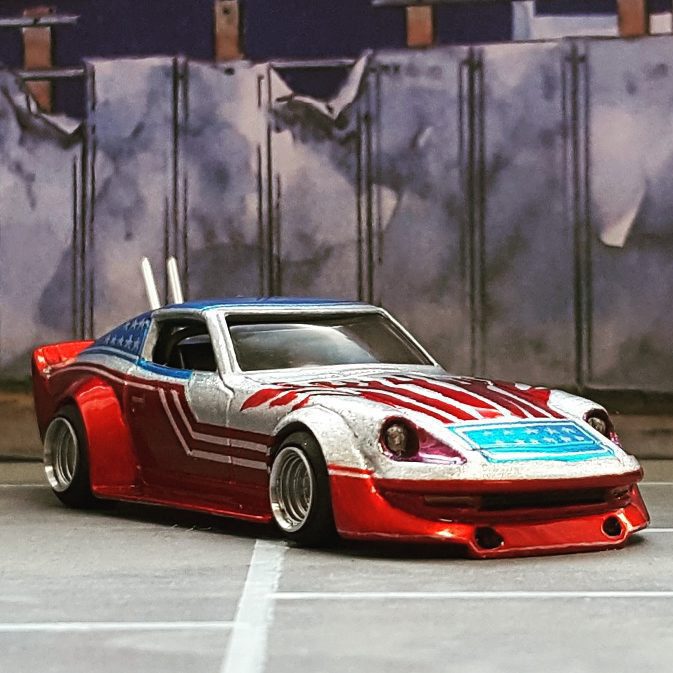 Diecast car with American flag paint job, parked in front of a graffiti-covered wall. Toy car model in urban setting.