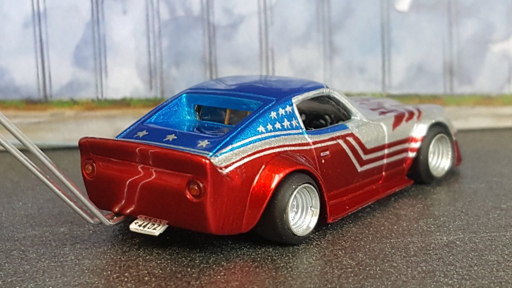 Red, silver, and blue toy car with stars and stripes design, parked on textured surface. License plate reads ナンバー 2402.
