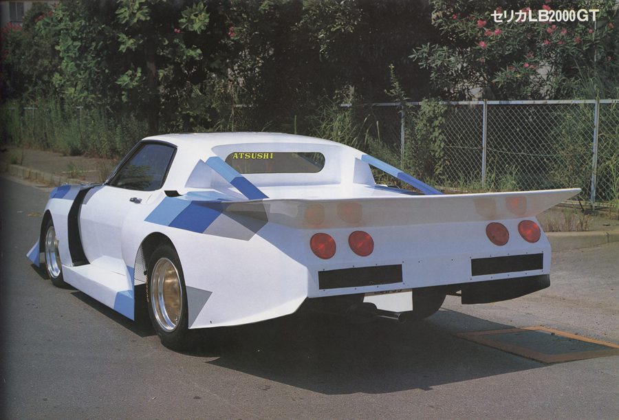 Customized Celica LB2000GT with bold rear spoiler design and Atsushi on the window, parked next to a fence.