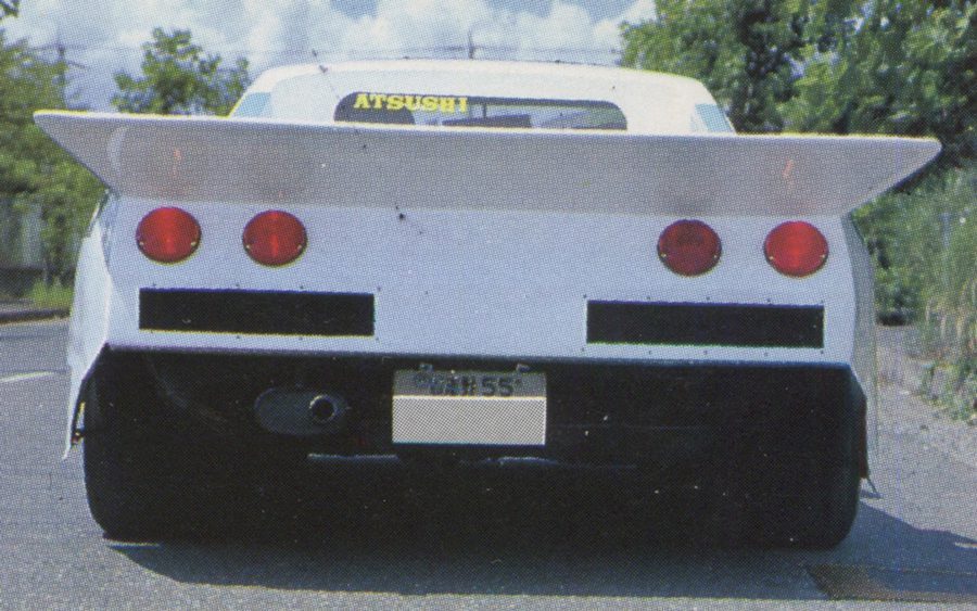 Rear view of a modified Bosozoku car with large spoiler and dual round tail lights, windshield sticker reading Atsushi, on street.
