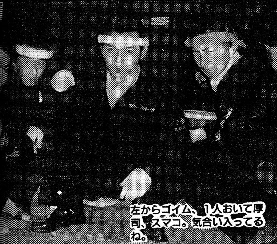 Three men wearing headbands and black jackets sitting closely in a dimly-lit room with Japanese text overlay.