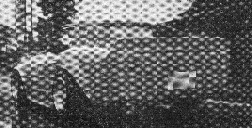 Retro Japanese sports car with a widebody kit driving on a rainy street.