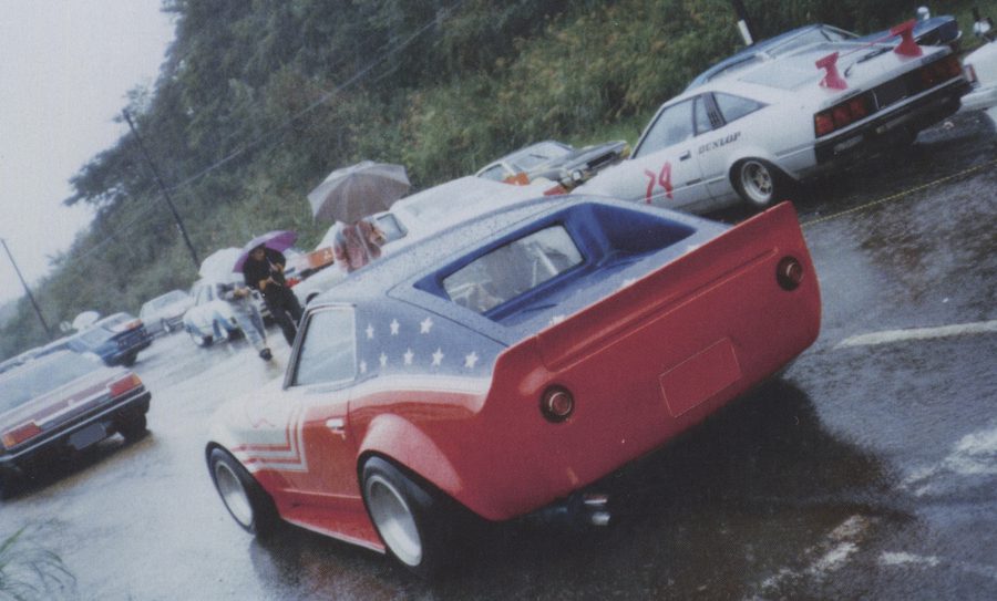 Modified classic cars in the rain, featuring American-themed bodywork and Japanese text ロケバニ (Rocket Bunny) and ダンロップ (Dunlop).