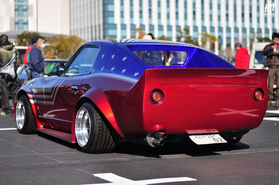 A vintage red and blue sports car with custom paint and wide tires, displayed at an outdoor car show in Japan.
