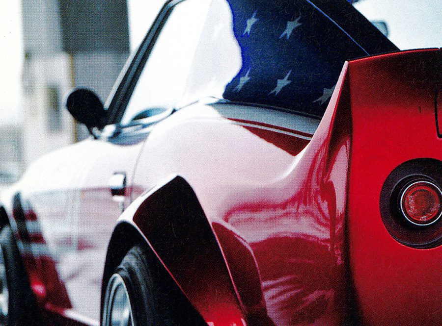 Close-up of a red sports car with a blue vinyl roof featuring white stars, highlighting its sleek curves and rear light.