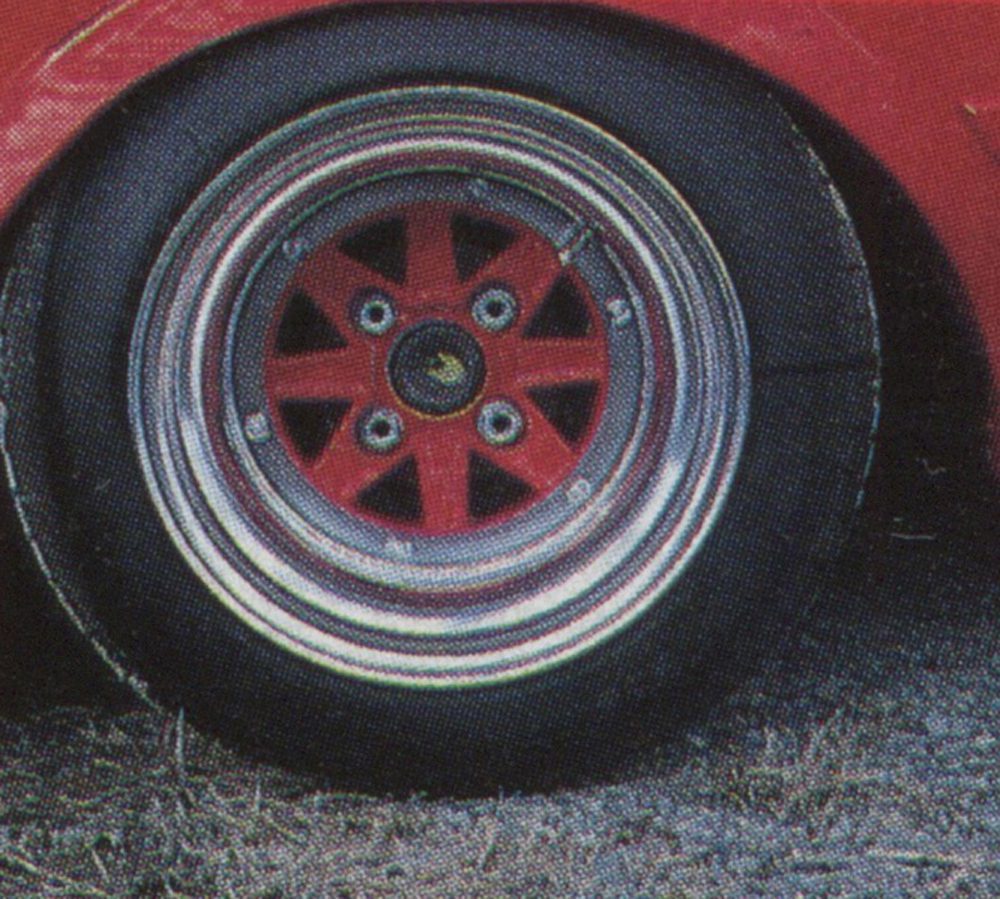 Close-up of a red and black car wheel with detailed rim design. Japanese characters 速度 on the tire, meaning speed.
