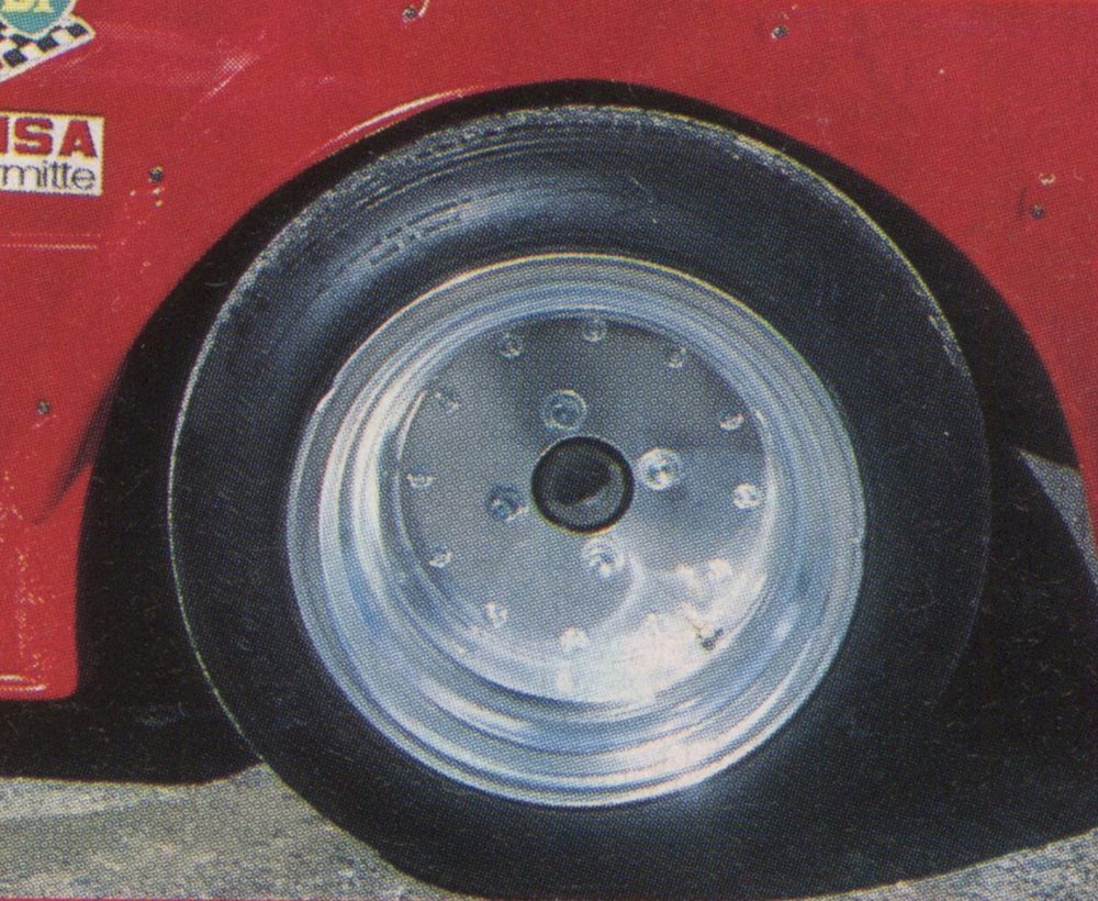 Close-up of a racing car's shiny aluminum wheel on a red vehicle. The tire is thick and designed for high performance racing.