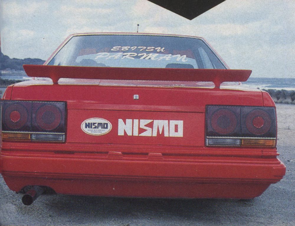 Rear view of a red NISMO car with Ebisu Parkman written on the rear windshield, parked by the seaside.
