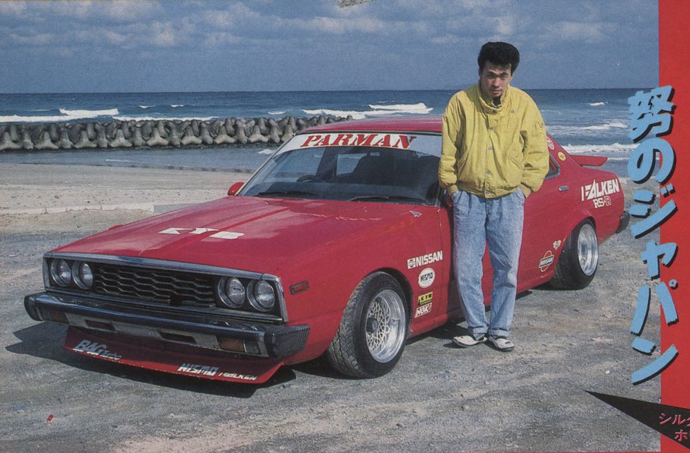 Man standing next to customized red Nissan car by the ocean, with Japanese text Dreams of Japan on the right.