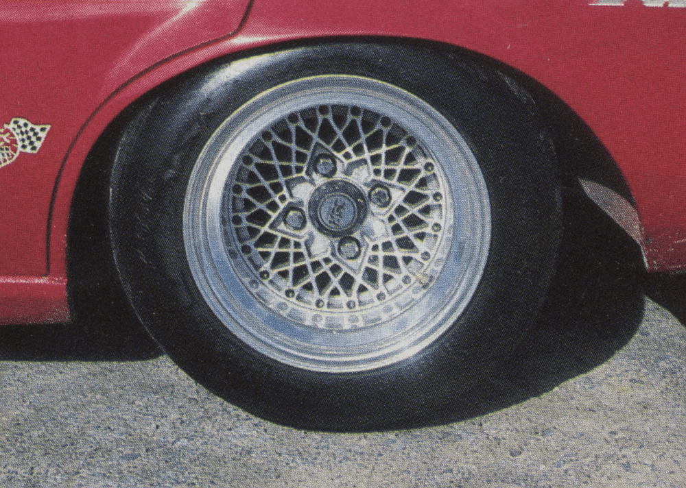 Close-up of a red race car's alloy wheel with intricate spoke design and a checkered flag decal.