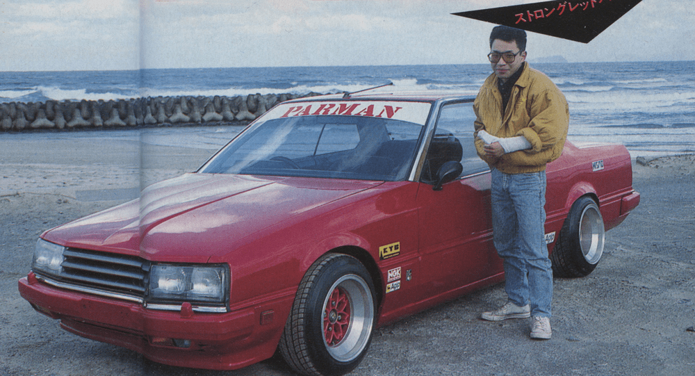 A man standing by a red modified car (PARMAN) on a beach. The Japanese text reads ストロングレット which translates to Strong Red.
