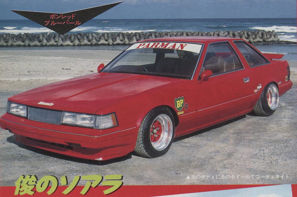 Vintage red sports car parked by the beach, showcasing bold Parman decal and BP logo. Translation: My Soarer.