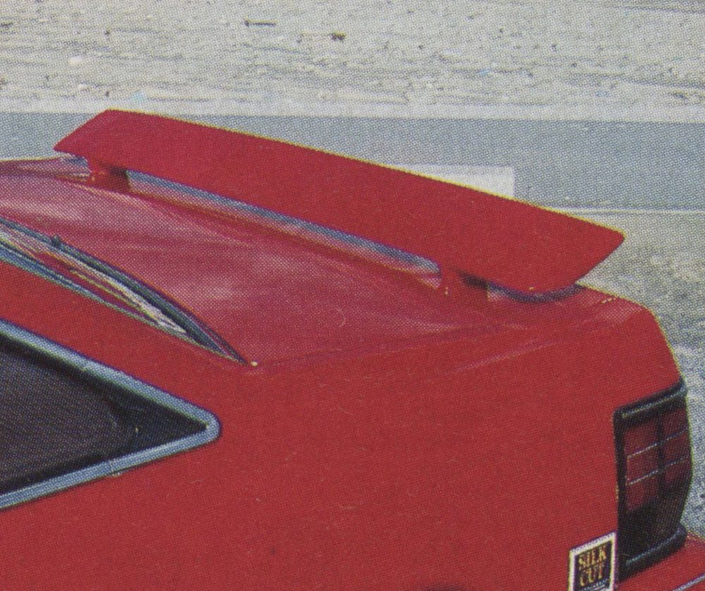 Close-up shot of a red sports car with a rear spoiler and 'Silk Cut' branding on the bumper.