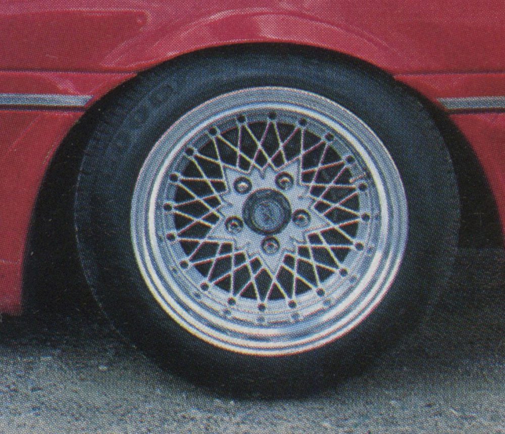 Close-up of a vintage car's alloy wheel and tire in excellent condition on a red vehicle.