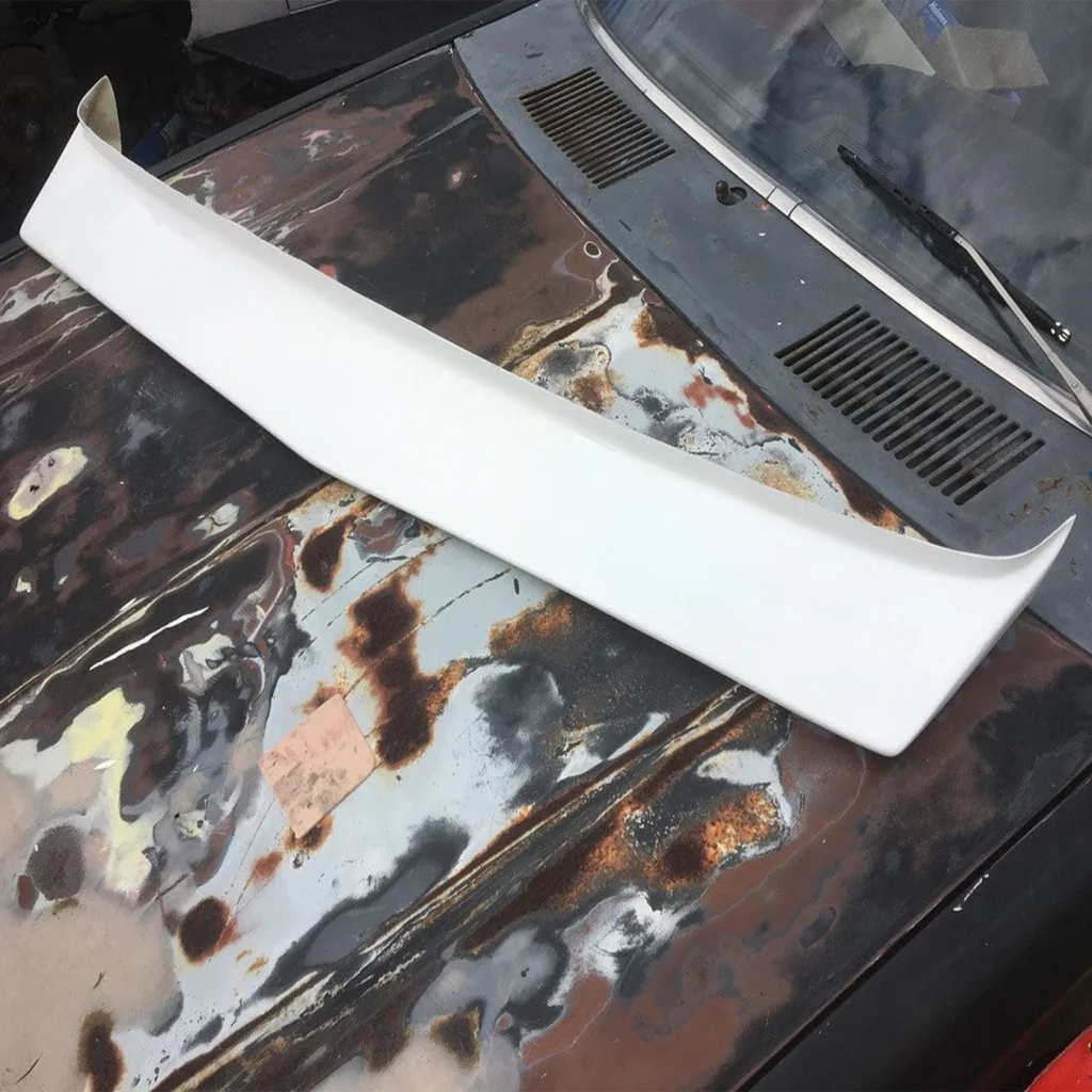 White car spoiler on heavily rusted and weathered car hood, showing contrast between new and old vehicle parts.