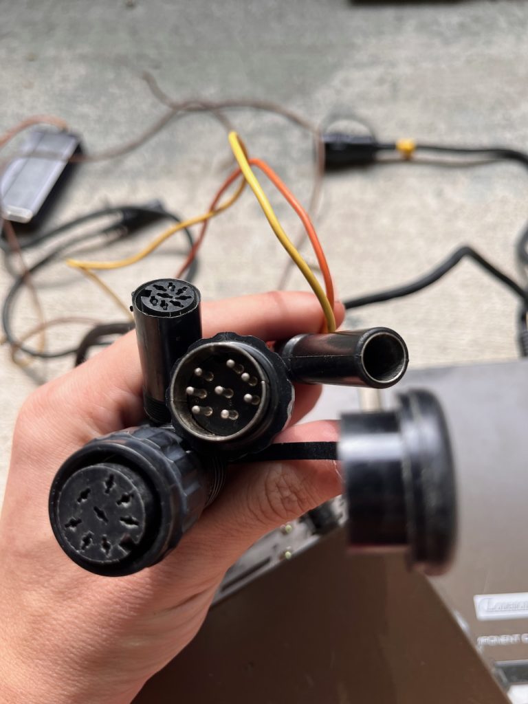 Close-up of a hand holding various cables and connectors with electronic devices in the background.