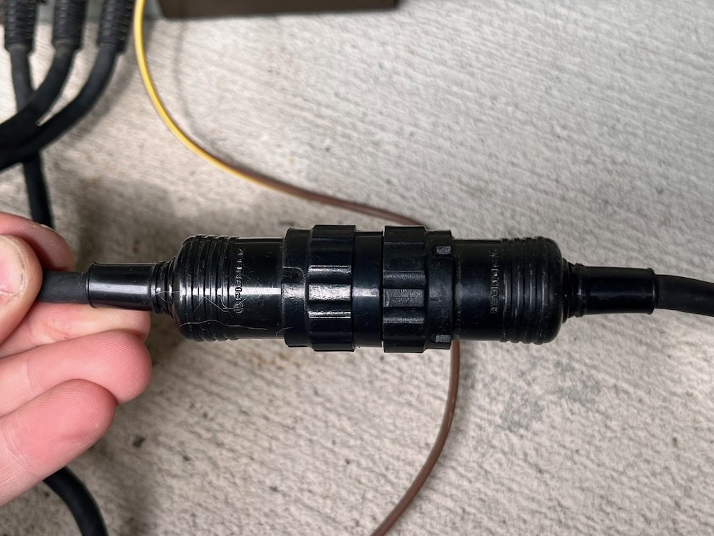 Close-up of a black waterproof electrical connector with Japanese text, held by a hand, multiple cables visible.