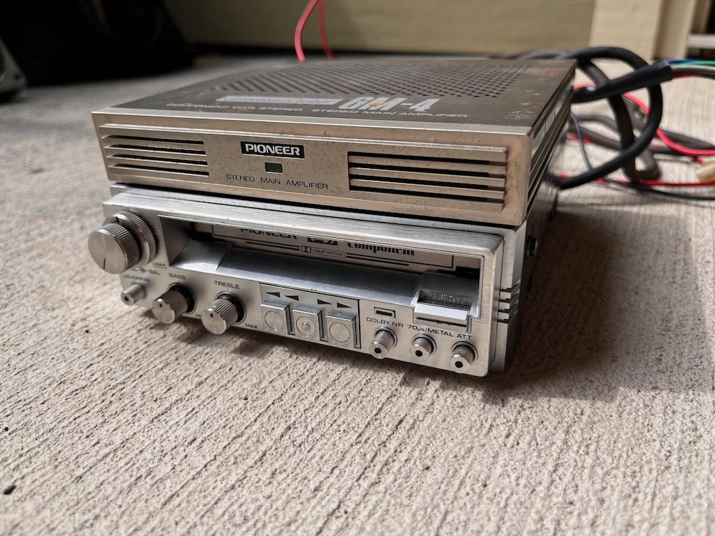 Vintage Pioneer stereo main amplifier and cassette player on concrete surface, featuring various control knobs and switches.