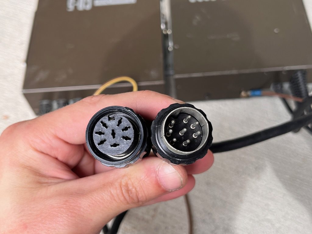 Hand holding a 7-pin and a 9-pin circular connector plug and receptacle used for electronic equipment connections.