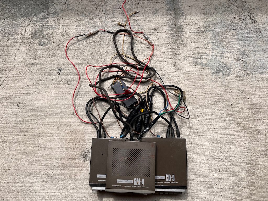 Vintage car stereo amplifier and graphic equalizer with tangled wires, labeled GM-4 and CD-5 on a concrete floor.