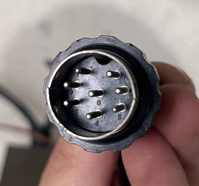 Close-up view of an 8-pin circular electrical connector held in hand for wiring or technical applications.