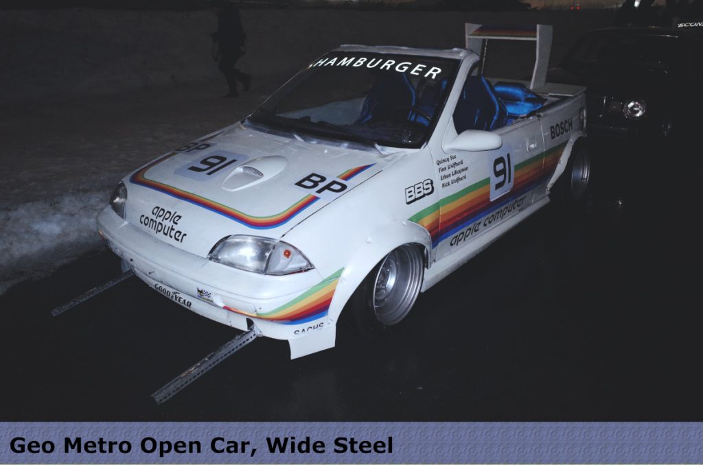 Modified Geo Metro convertible with Apple Computer branding, custom wide steel wheels, and rainbow stripes in snow.