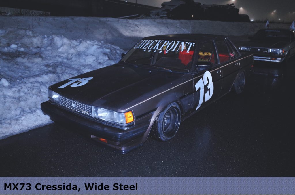 Vintage MX73 Cressida car with '73' number decal and 'CHECKPOINT' on the windshield parked beside icy road.