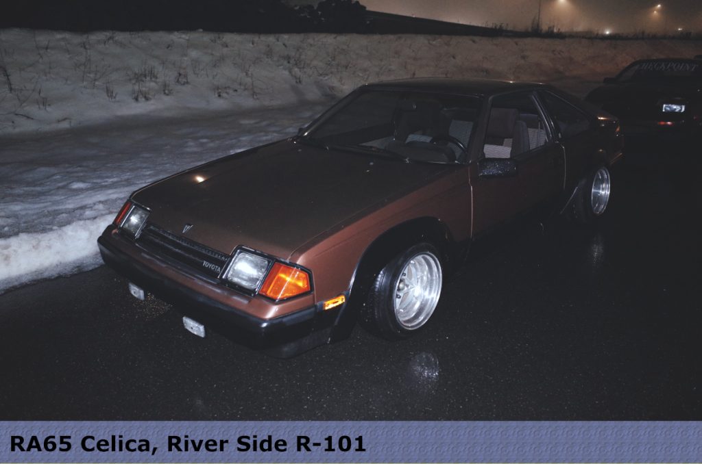 Brown 1985 Toyota Celica RA65 on a wet road at night near a snow-covered embankment.