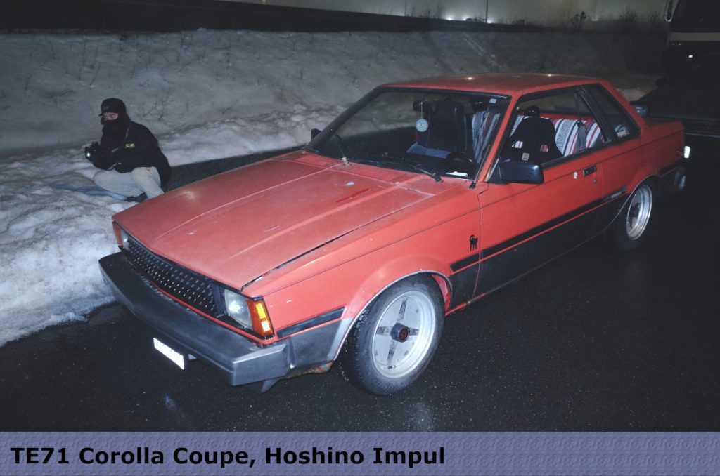 TE71 Corolla Coupe with Hoshino Impul wheels on a snowy night, person crouching beside car.