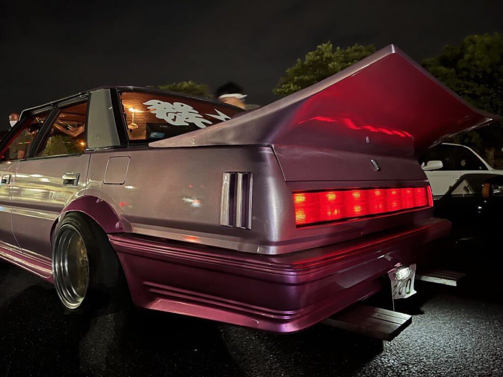 Vintage car with large spoiler and custom rims at night car meet.