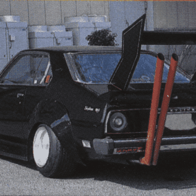 Modified classic black car with large rear wing and dual exhaust pipes for a unique street racing style.