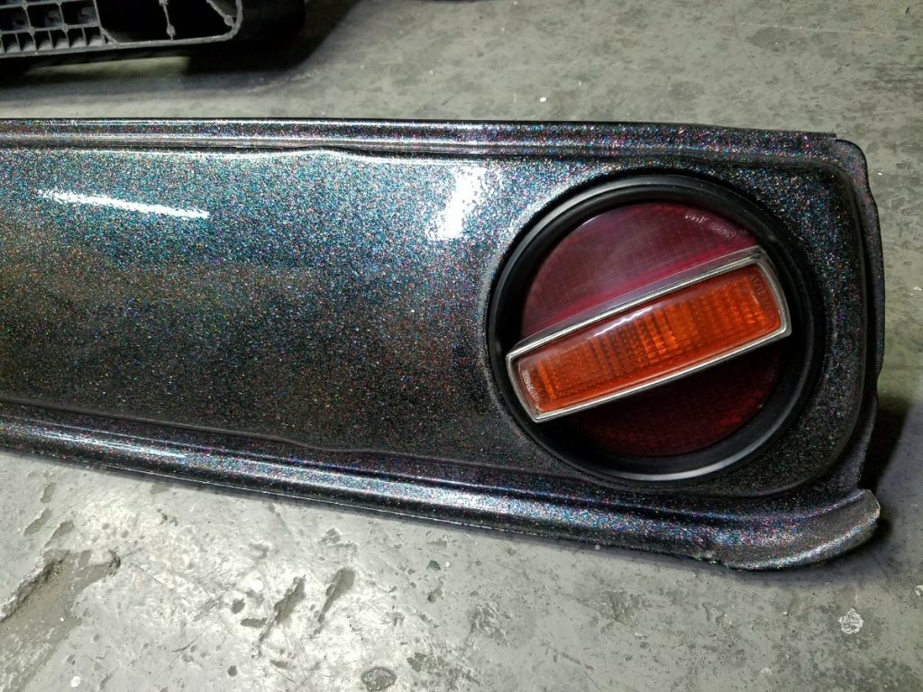 Close-up of a sparkling car tail light with a glossy multicolor finish, featuring both red and orange sections.