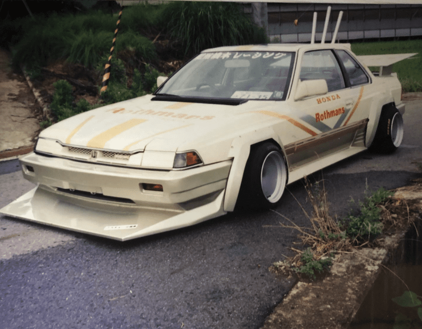 Modified Honda car with Rothmans and レースカー (racecar) decals, wide body kit, and custom wheels, parked outdoors.