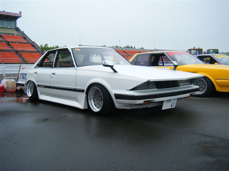 White modified car with number plate 61 on a wet track, parked beside a yellow car. Japanese kanji reads 練習 meaning practice.