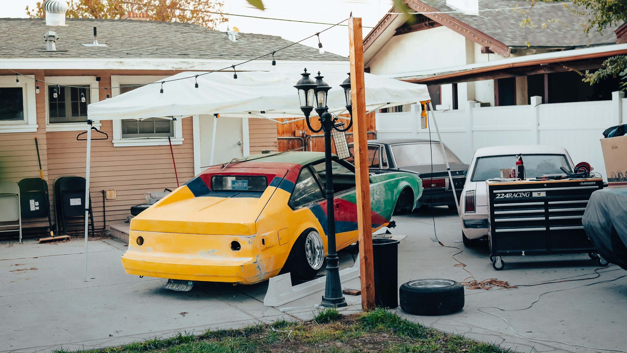 Backyard workshop with colorful modified cars, a canopy, and a toolbox labeled 22-4 Racing. Ready for restoration work.