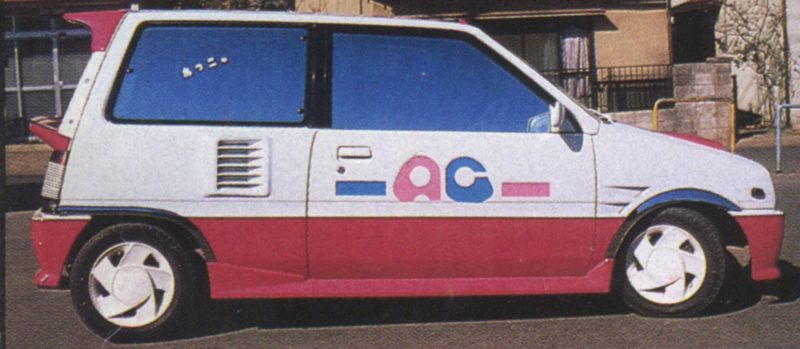 Vintage white and pink hatchback car with unique おつき (Otsuki) Japanese text and AC logo parked on the street.