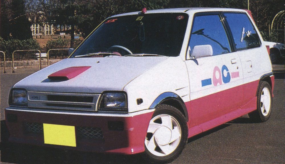 A vintage white and pink customized hatchback kei car parked on a street in Japan during the day.