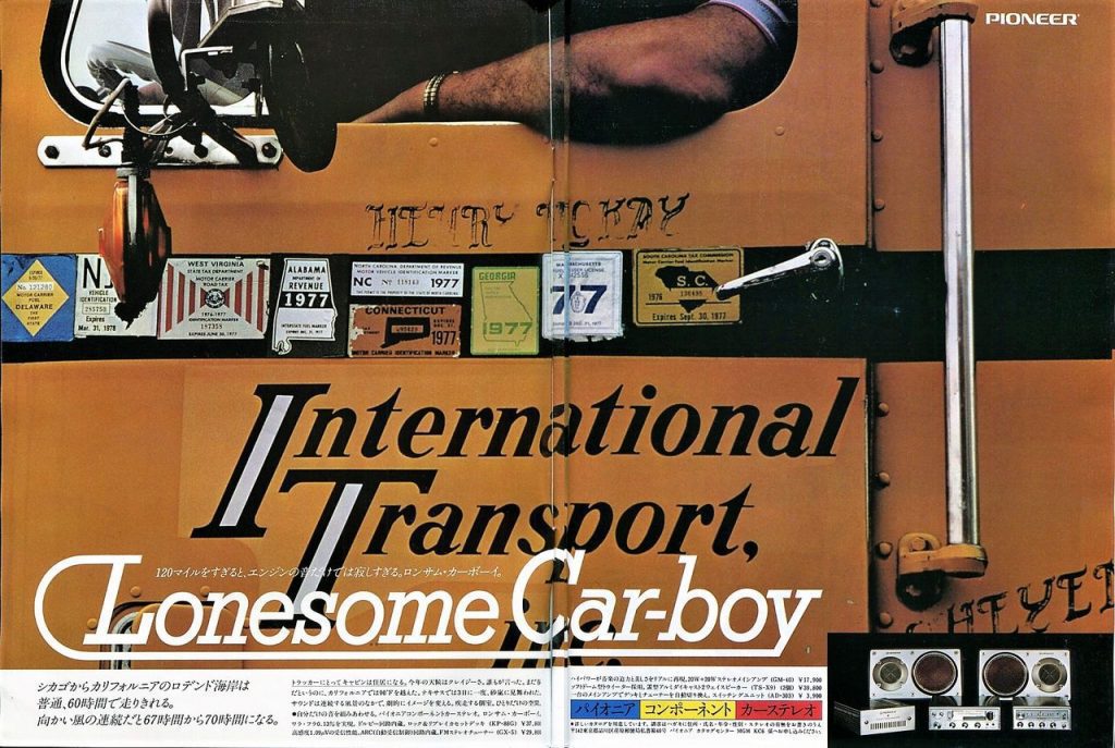 Close-up of a yellow truck with various state stickers and text International Transport, Lonesome Car-boy in Japanese.