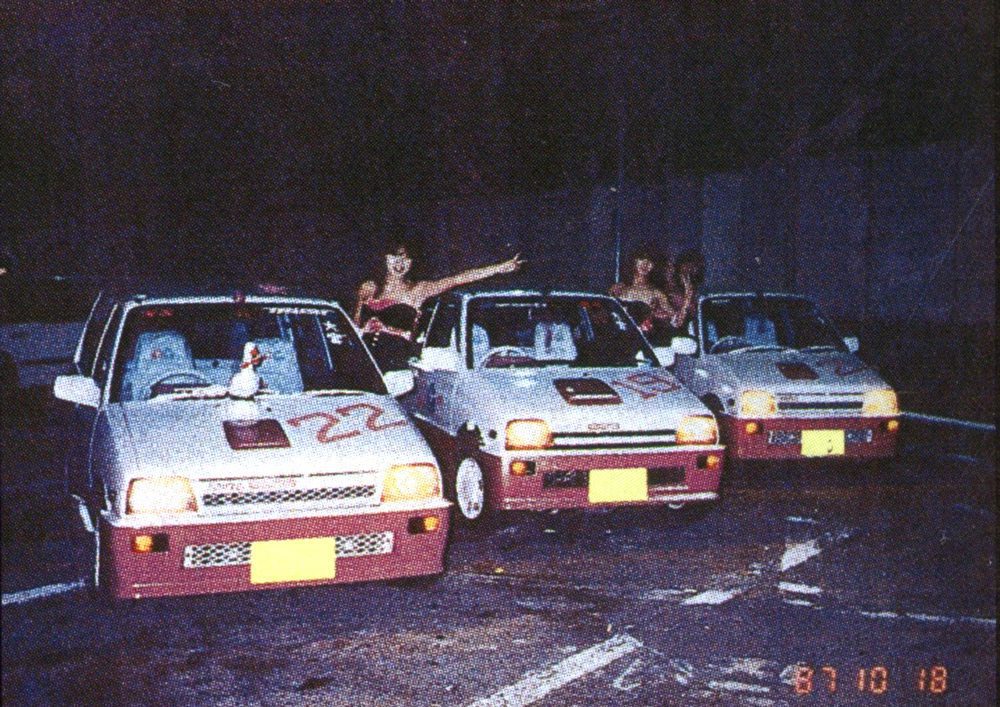 Vintage scene with three modified cars in Japan, adorned with numbers and decals, dated October 18, 1987.