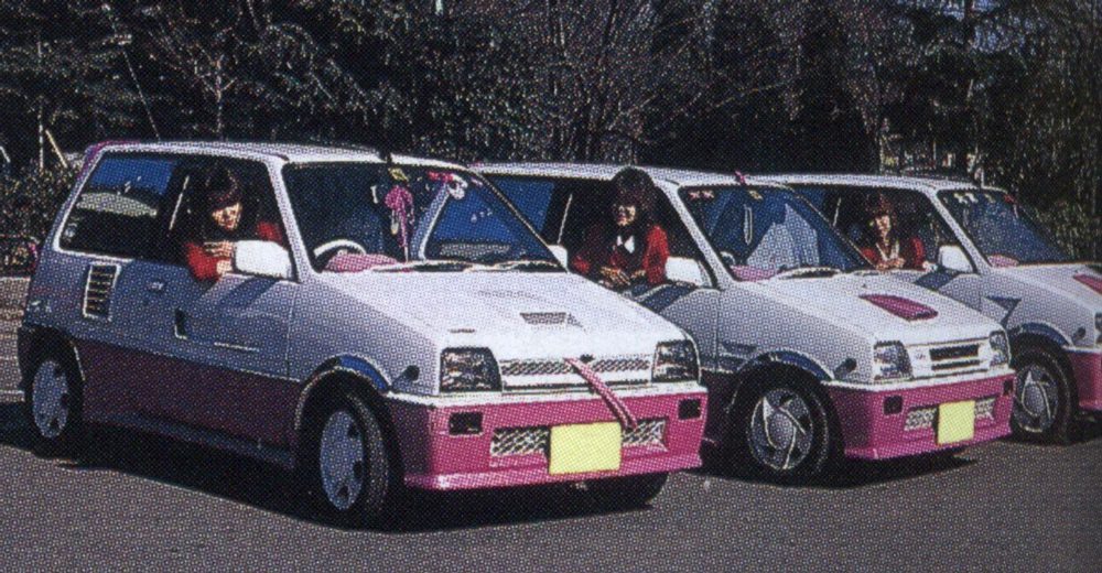 Three women driving pink and white decorated retro cars.