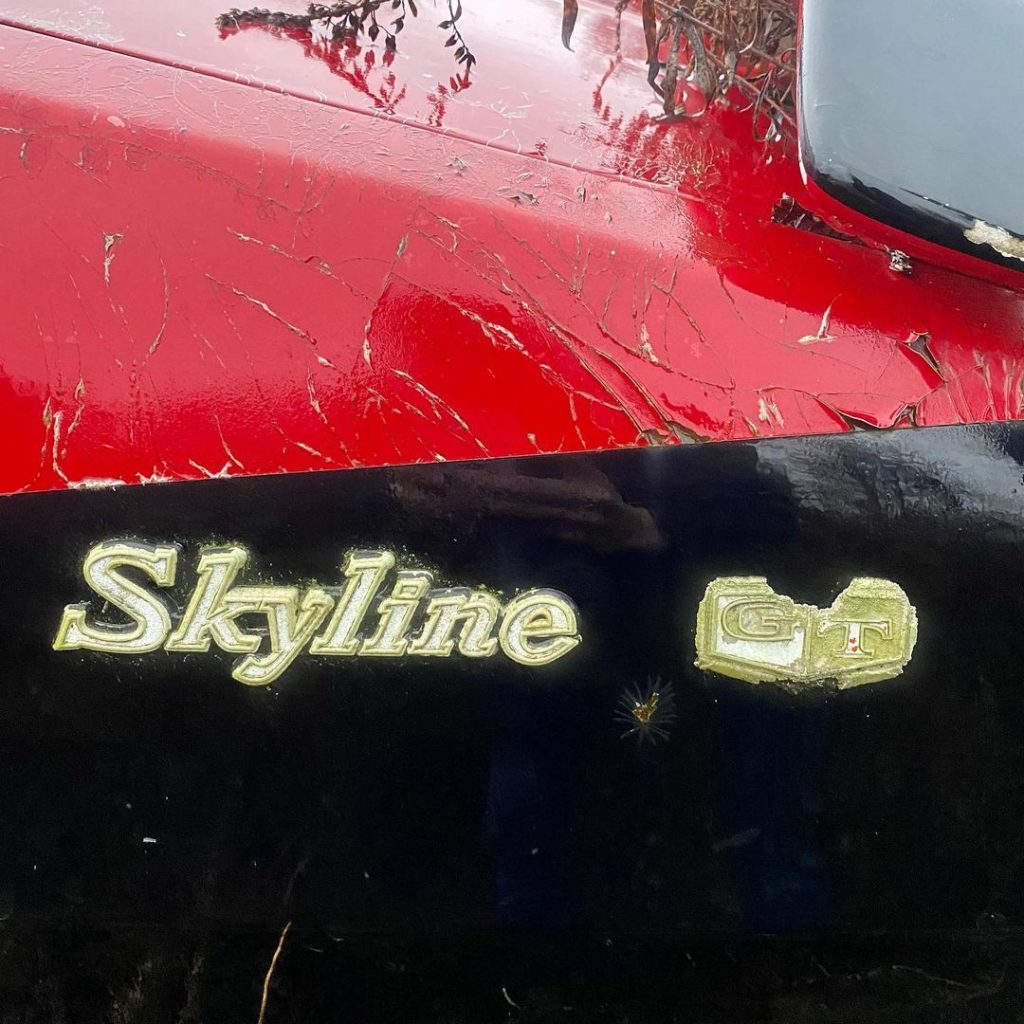 Close-up of Nissan Skyline GT badge on a black and red car. The GT badge is worn. High-performance sports car.