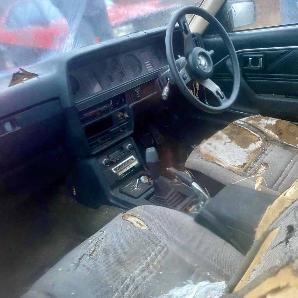 Interior of a weathered vintage car with torn seats and an old Japanese stereo, showcasing signs of significant wear and age.