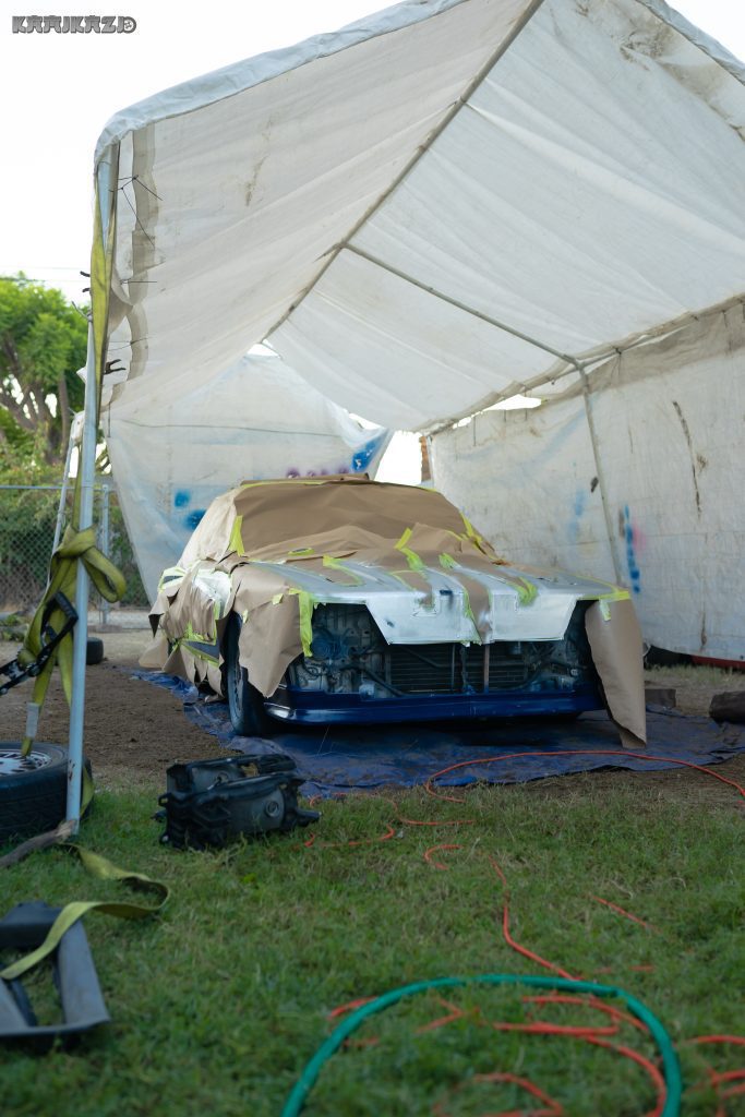 Partially covered car under a canopy for painting, with the word KAMIKAZE in Japanese at the top of the image.