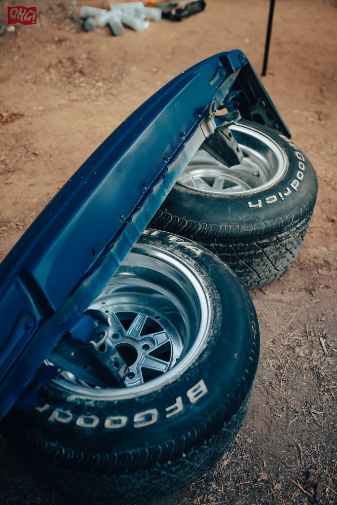 Two car tires with metallic rims and a blue car fender lying on the ground, featuring BF Goodrich tires.
